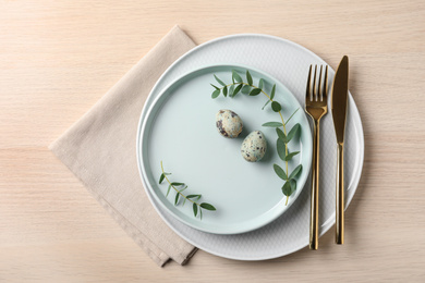 Festive Easter table setting with quail eggs on wooden background, flat lay.