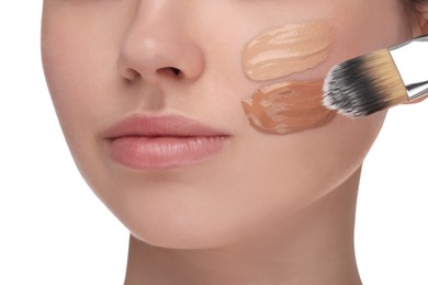 Photo of Teenage girl applying foundation on face with brush against white background, closeup