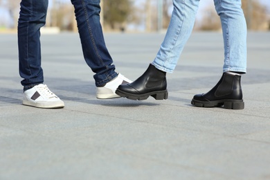 Photo of People greeting each other by bumping feet instead of handshake outdoors, closeup