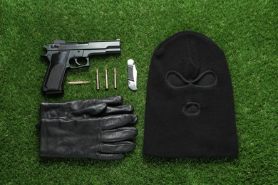 Flat lay composition with balaclava and weapons on green grass