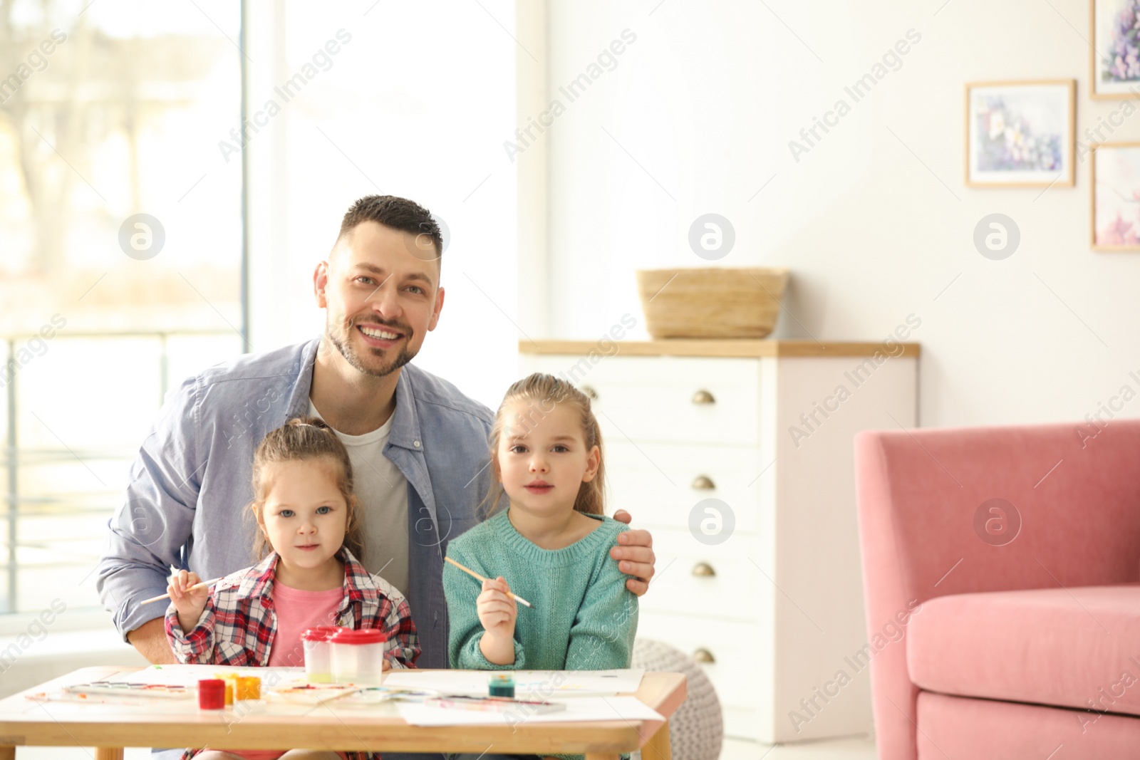 Photo of Father and daughters painting at table indoors. Playing with children