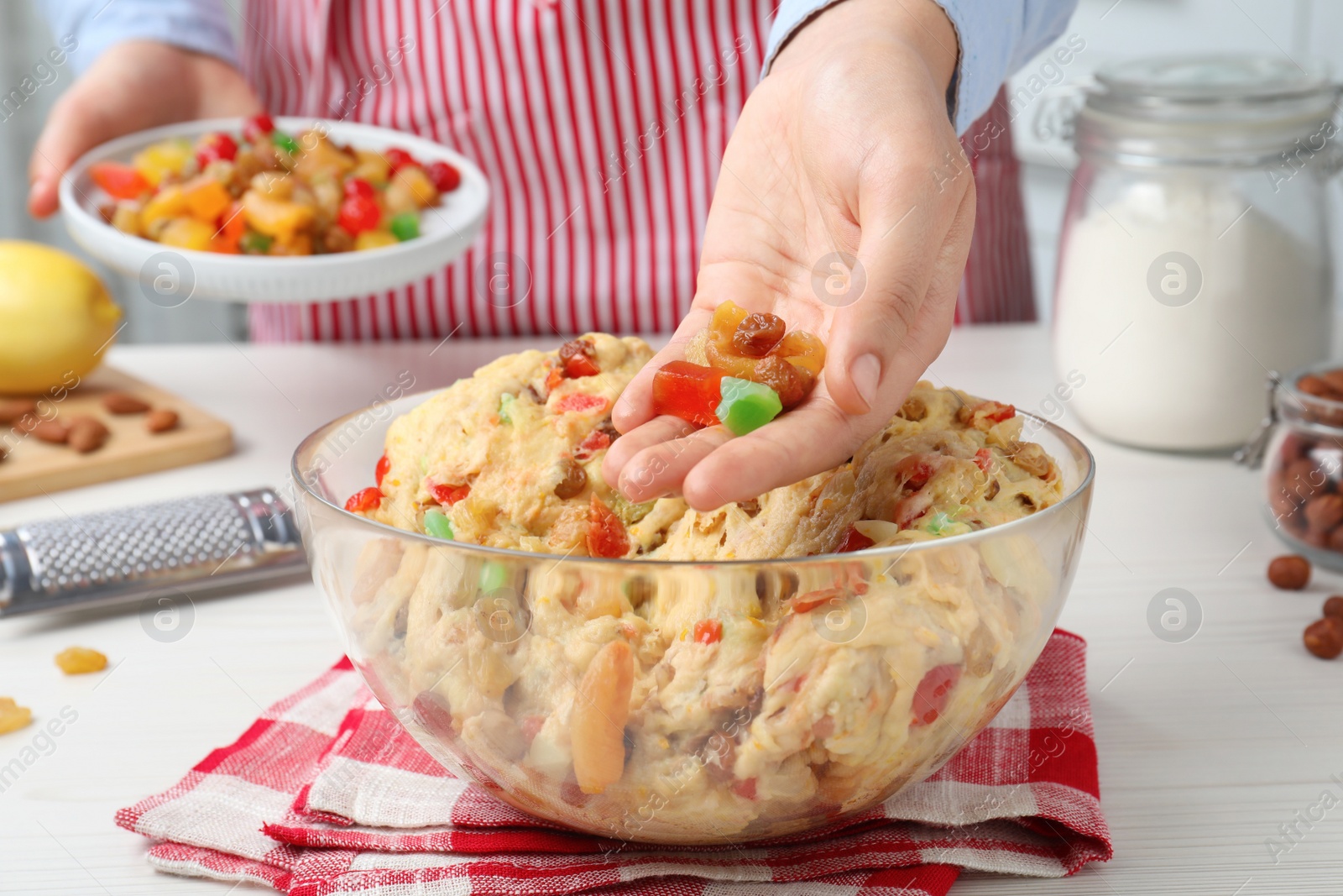 Photo of Woman adding candied fruits to dough for Stollen at white wooden table, closeup. Baking traditional German Christmas bread