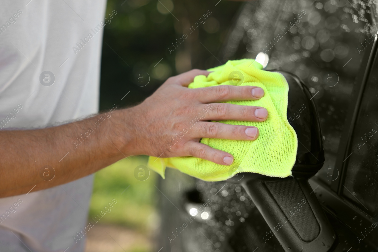 Photo of Man washing car side mirror with rag outdoors, closeup
