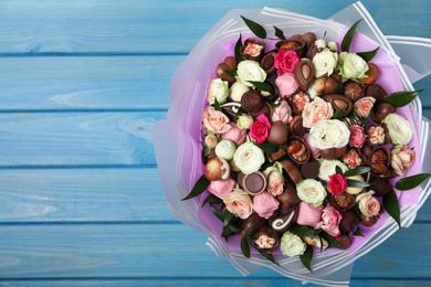 Photo of Beautiful bouquet of flowers and chocolate candies on light blue wooden table, top view. Space for text
