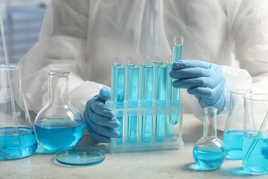 Photo of Scientist taking test tube with light blue liquid at white table in laboratory, closeup
