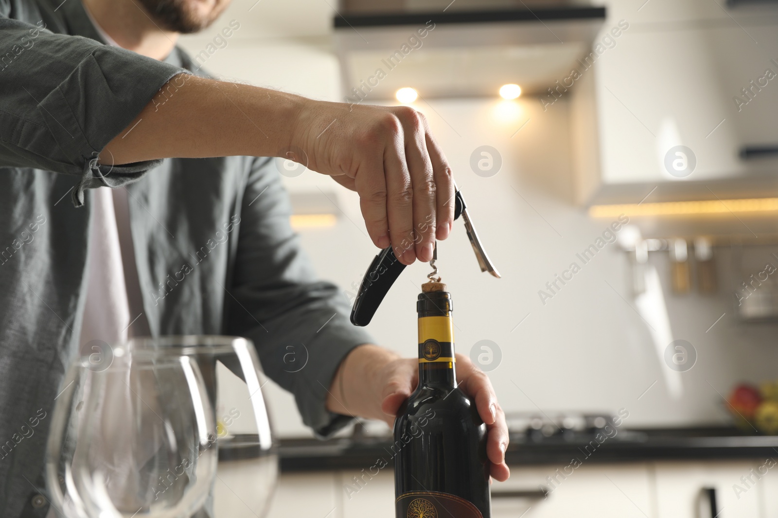 Photo of Man opening wine bottle with corkscrew indoors, closeup. Space for text