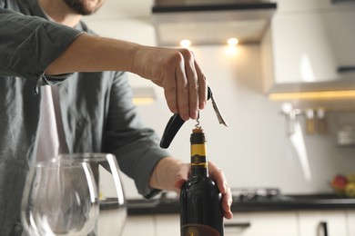 Man opening wine bottle with corkscrew indoors, closeup. Space for text