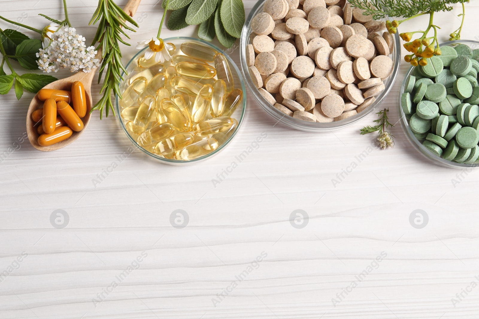 Photo of Different pills, flowers and herbs on white wooden table, flat lay with space for text. Dietary supplements