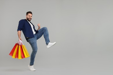 Photo of Excited man with many paper shopping bags on grey background. Space for text