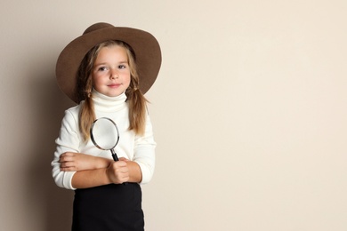 Cute little child in hat with magnifying glass playing detective on beige background, space for text