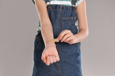Photo of Girl putting sticking plaster onto wrist against light grey background, closeup