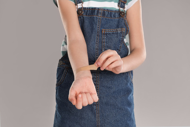 Girl putting sticking plaster onto wrist against light grey background, closeup