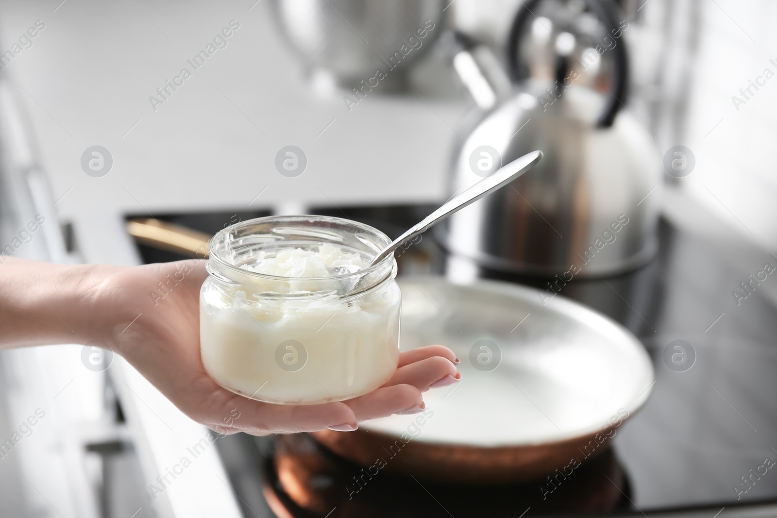 Photo of Woman holding jar with coconut oil near kitchen stove