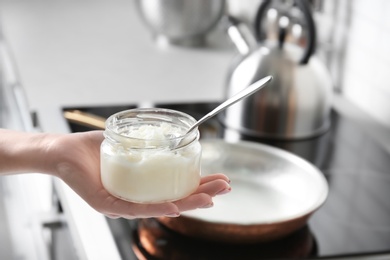 Woman holding jar with coconut oil near kitchen stove