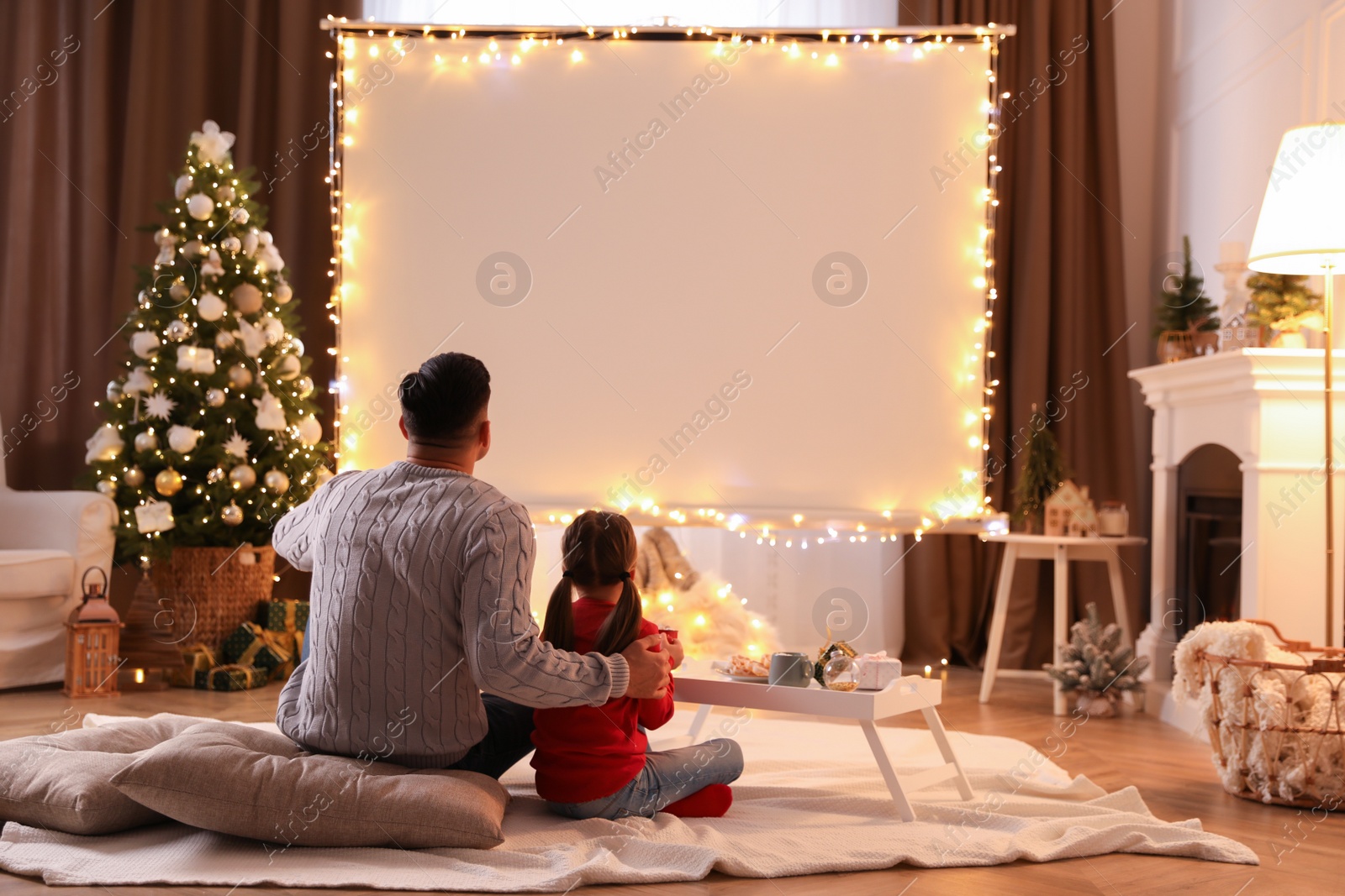 Photo of Father and daughter watching movie using video projector at home. Cozy Christmas atmosphere