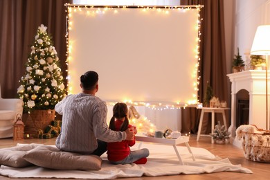 Father and daughter watching movie using video projector at home. Cozy Christmas atmosphere