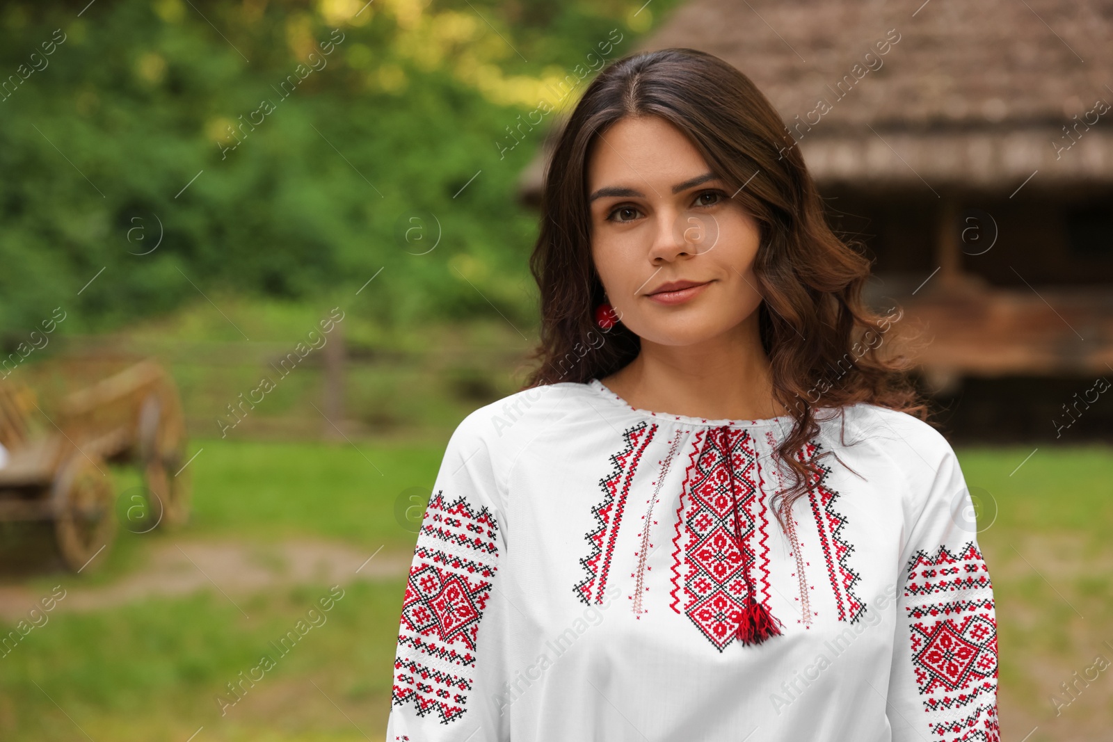 Photo of Beautiful woman wearing embroidered shirt in village, space for text. Ukrainian national clothes