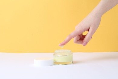 Woman with jar of cream on yellow background, closeup