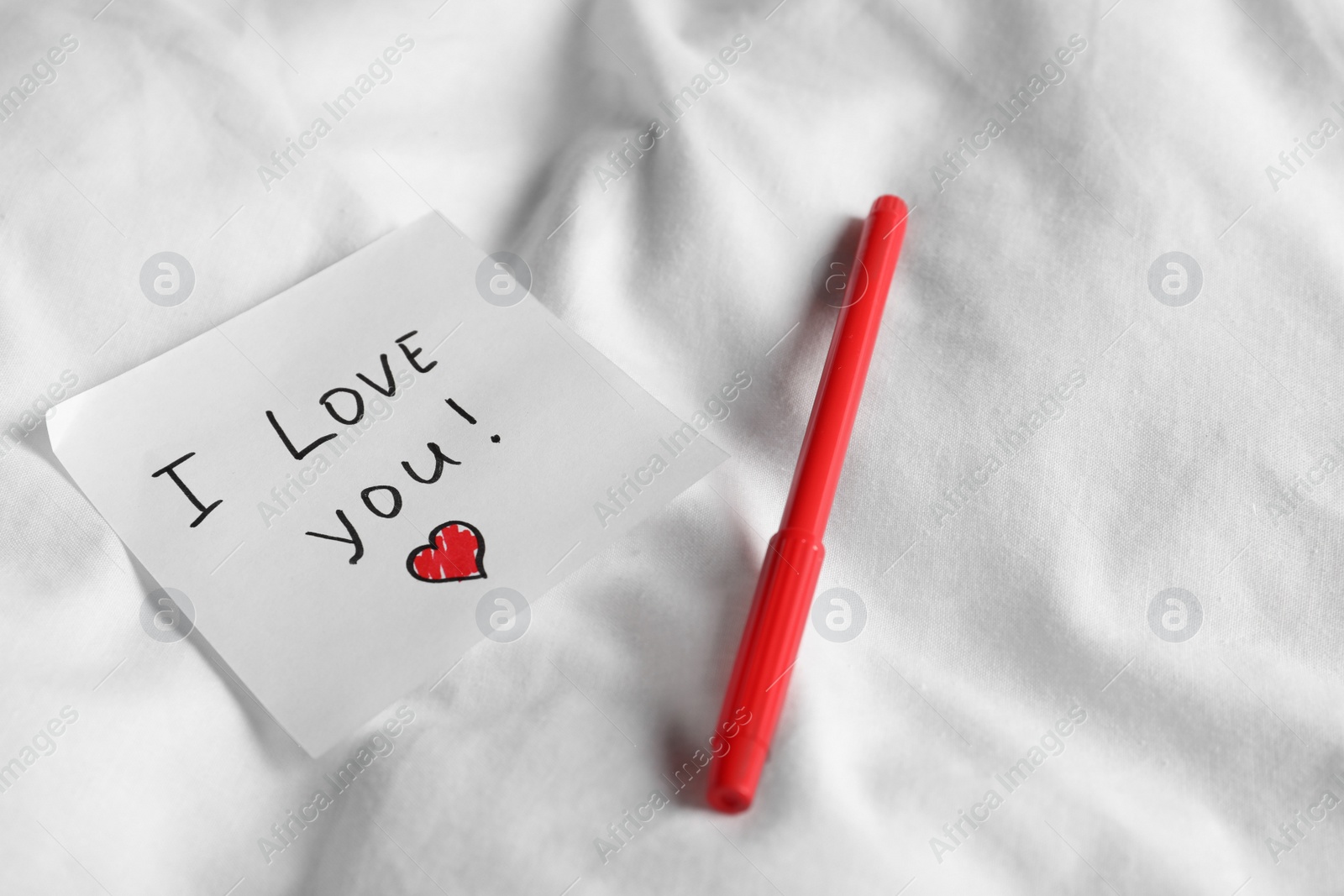 Photo of Sticky note with phrase I love you! and red felt pen on bed, space for text