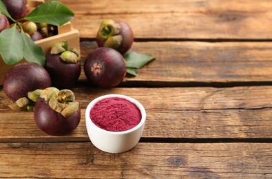 Photo of Purple mangosteen powder and fruits on wooden table. Space for text