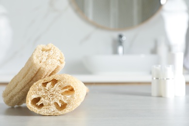 Photo of Natural loofah sponges on table in bathroom. Space for text