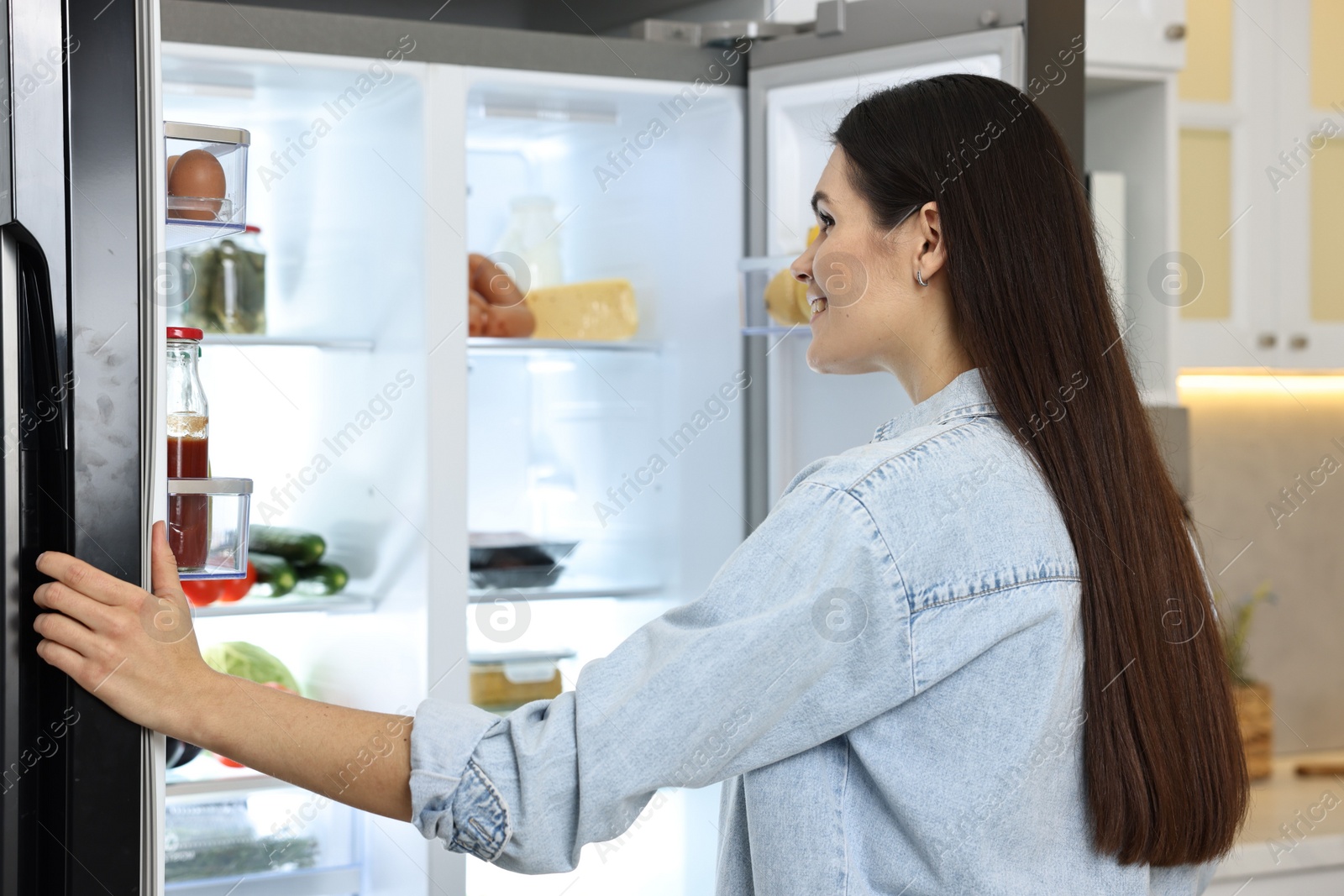 Photo of Young woman near modern refrigerator in kitchen