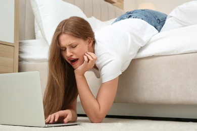 Photo of Lazy young woman using laptop while lying on bed at home