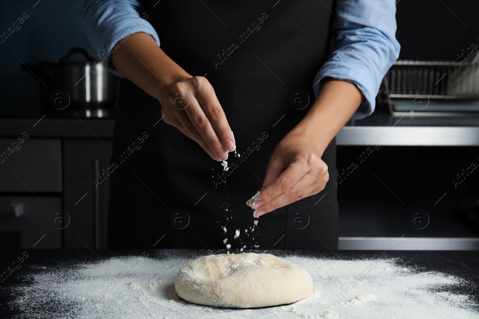 Photo of Woman sprinkling dough for pastry with flour on table