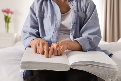 Photo of Blind senior person reading book written in Braille on bed indoors, closeup