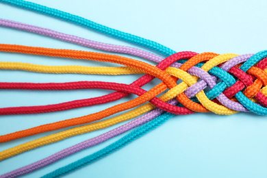 Photo of Braided colorful ropes on light blue background, top view. Unity concept