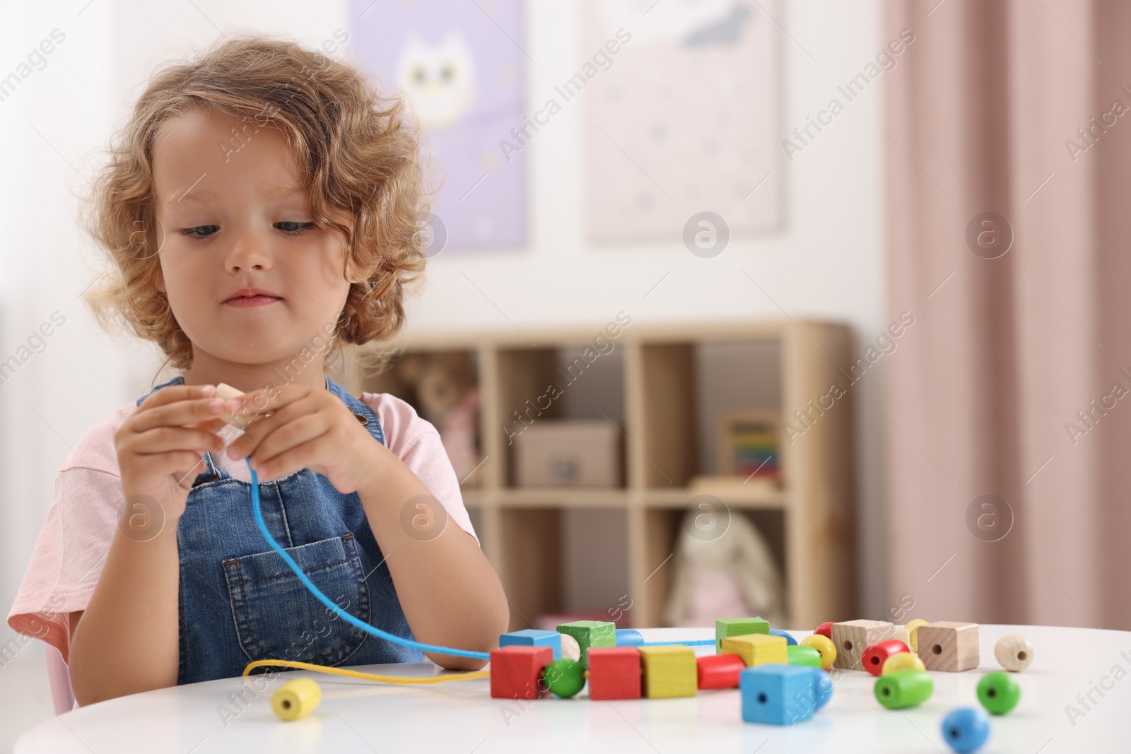 Photo of Motor skills development. Little girl playing with wooden pieces and string for threading activity at table indoors