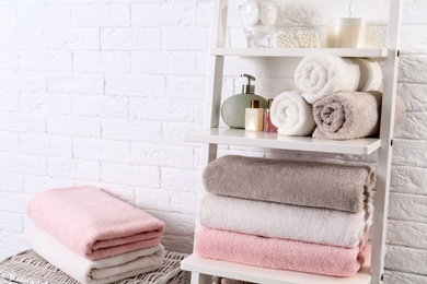 Photo of Shelving unit with clean towels and toiletries near brick wall