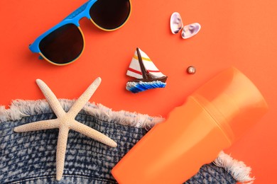 Flat lay composition with bottle of sunscreen on coral background