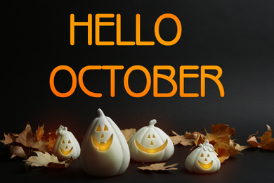 Image of Hello October card. Jack-o-Lantern candle holders as Halloween decor and autumn dry leaves on black table