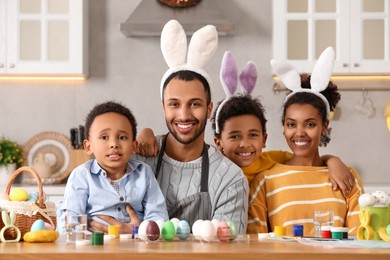 Photo of Happy African American family with Easter eggs at table in kitchen