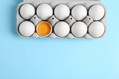 Photo of Fresh chicken eggs in box on light blue background, top view. Space for text