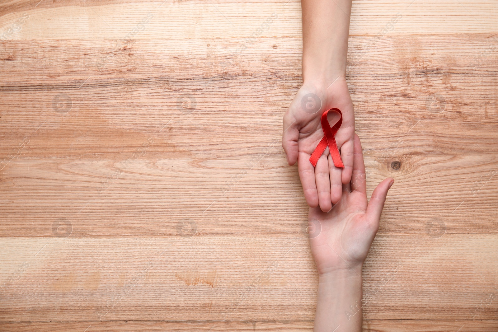 Photo of Women holding red awareness ribbon on wooden background, top view with space for text. World AIDS disease day