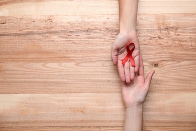 Photo of Women holding red awareness ribbon on wooden background, top view with space for text. World AIDS disease day
