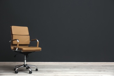 Comfortable office chair near black wall indoors. Space for text