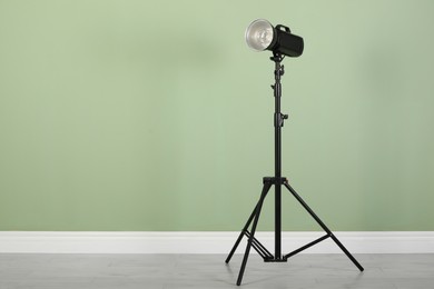 Photo of Studio flash light with reflector on tripod near pale green wall in room, space for text. Professional photographer's equipment