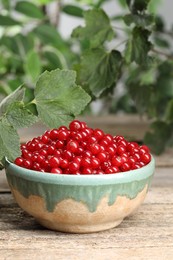 Ripe red currants in bowl on wooden table. Space for text