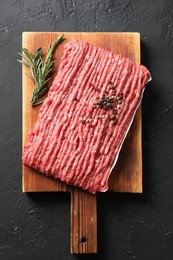 Raw ground meat, rosemary and peppercorns on black table, top view