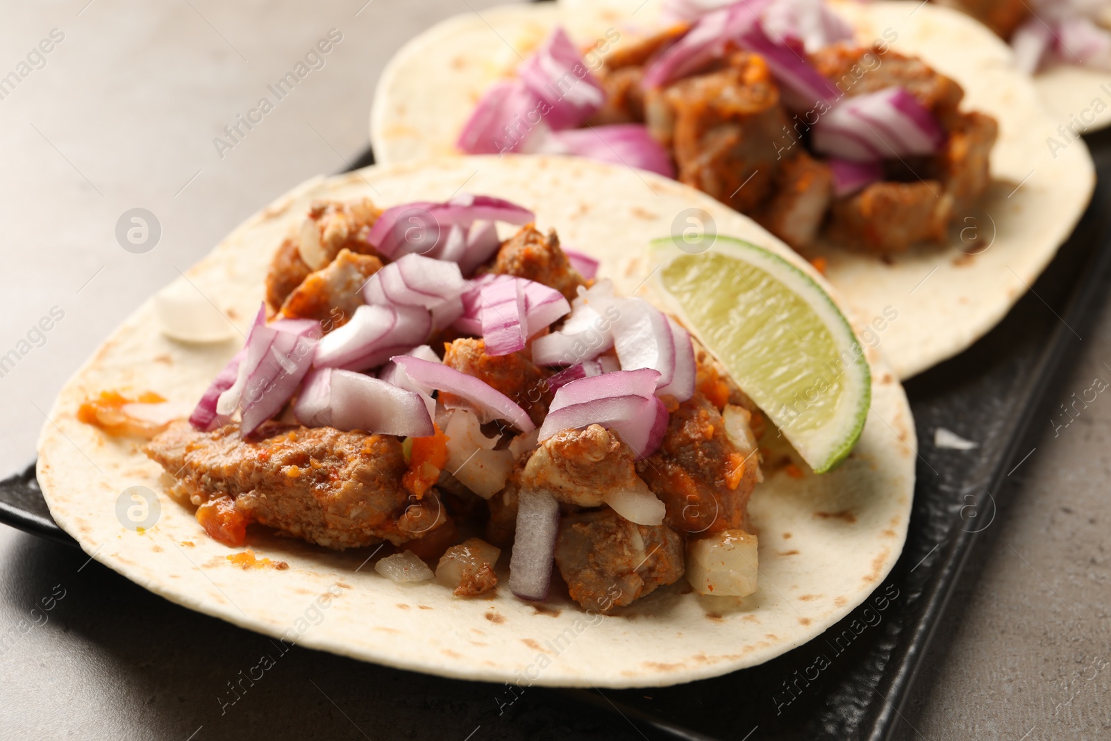 Photo of Delicious tacos with vegetables, meat and lime on grey table, closeup