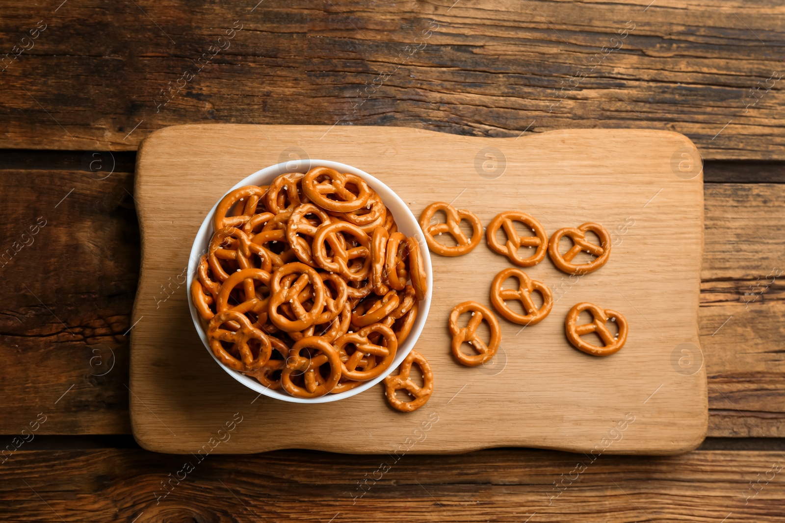 Photo of Bowl with delicious pretzel crackers on wooden table, top view