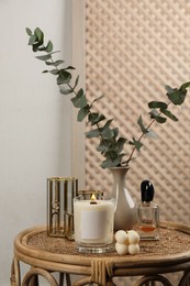 Burning soy candle, perfume and stylish accessories on wicker table indoors