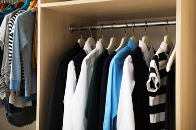 Photo of Hangers with teenage clothes on rack in wardrobe, closeup