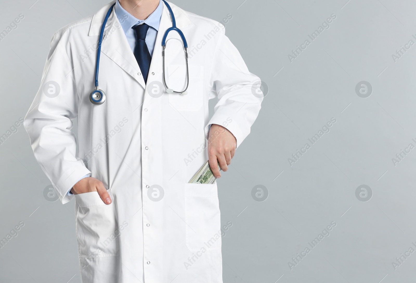 Photo of Doctor putting bribe money into pocket on grey background, closeup. Corruption in medicine