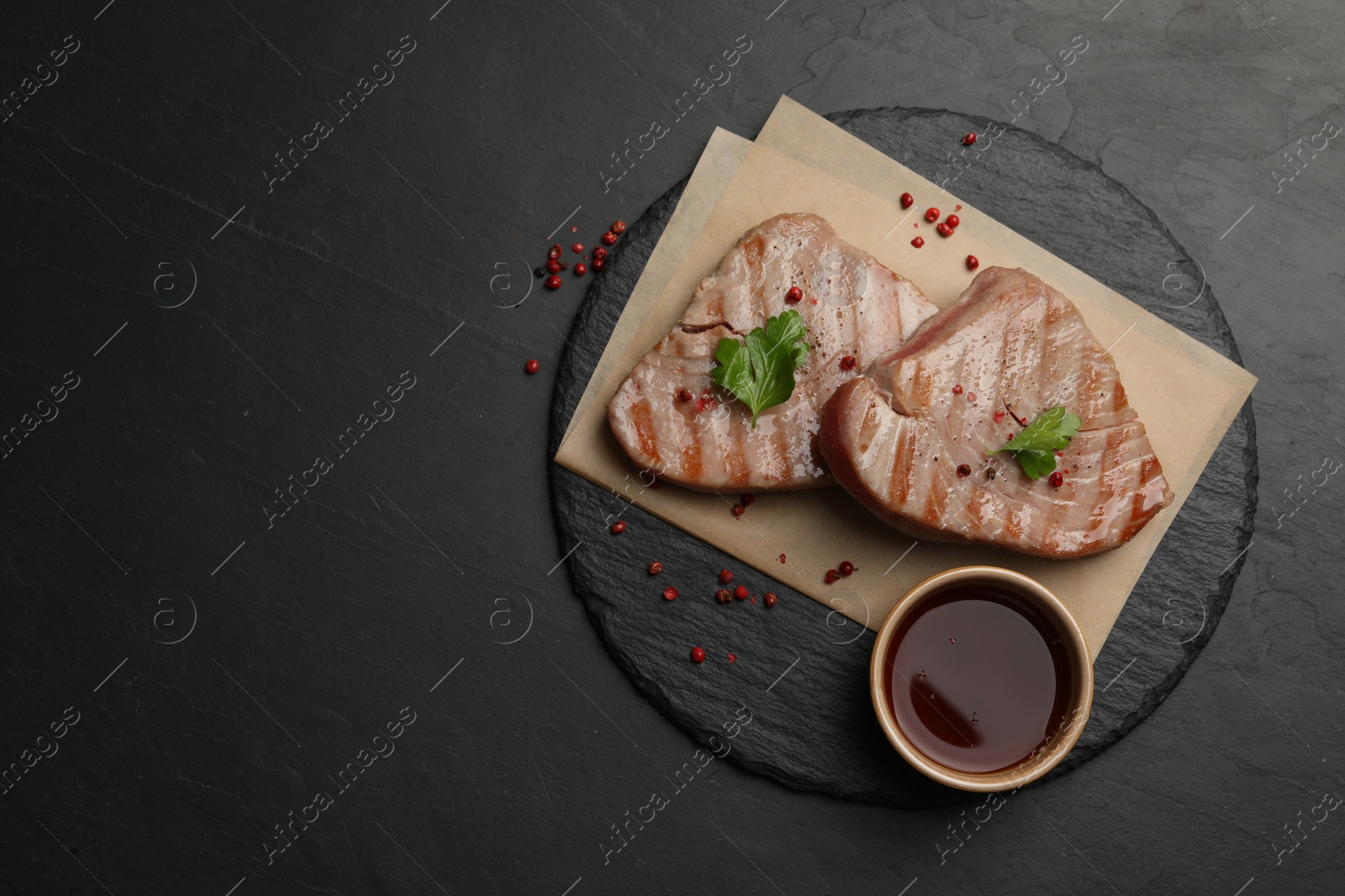 Photo of Delicious tuna steaks with sauce, parsley and spices on black table, top view. Space for text