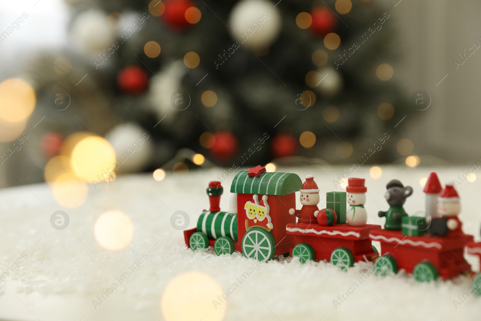 Photo of Bright toy train on artificial snow in room with Christmas tree