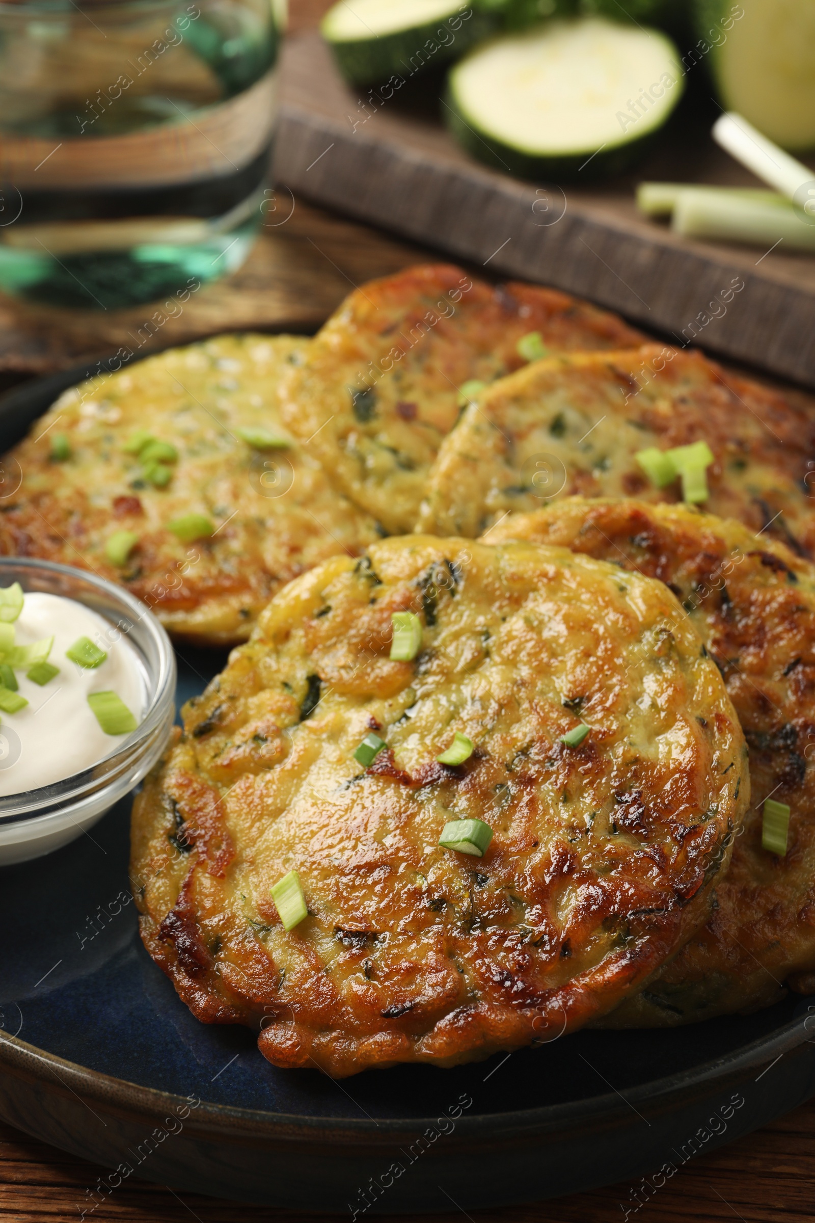 Photo of Delicious zucchini fritters with sour cream served on table, closeup